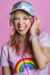 Porträt einer jungen Frau, die mit Kopfhörern vor einem rosa Hintergrund Musik hört und die Zunge herausstreckt - MGIF00101