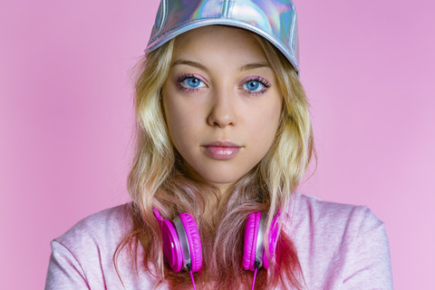 Portrait of young woman with headphones and basecap in front of pink background stock photo