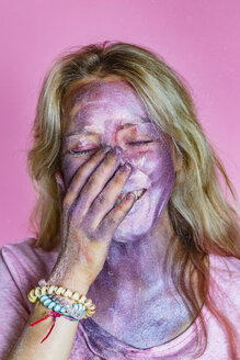 Porträt einer lachenden jungen Frau mit metallischem Schimmer im Gesicht vor einem rosa Hintergrund - MGIF00112