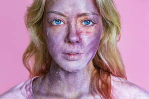 Porträt einer jungen Frau mit metallischem Schimmer im Gesicht vor einem rosa Hintergrund - MGIF00113