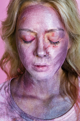 Porträt einer jungen Frau mit metallischem Schimmer im Gesicht vor einem rosa Hintergrund, lizenzfreies Stockfoto