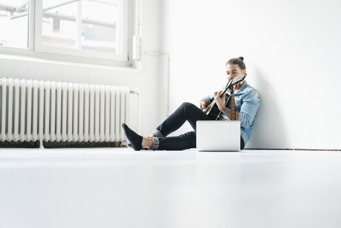 Mann sitzt mit Laptop auf dem Boden und spielt Gitarre - JOSF01528