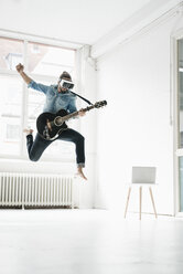 Mann mit Gitarre und Virtual-Reality-Brille springt in einem Loft in die Luft - JOSF01535