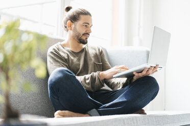 Portrait of man sitting on the couch using laptop - JOSF01543