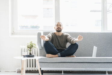 Portrait of man with eyes closed sitting on the couch doing yoga exercise - JOSF01544