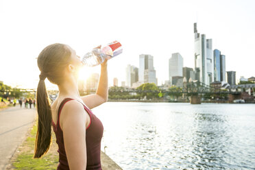 Deutschland, Frankfurt, sportliche junge Frau trinkt aus einer Flasche am Flussufer - PUF00704