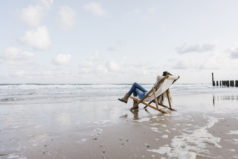 Frau sitzt auf einem Liegestuhl am Strand - KNSF02540