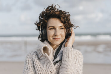Smiling woman on the beach with headphones - KNSF02557