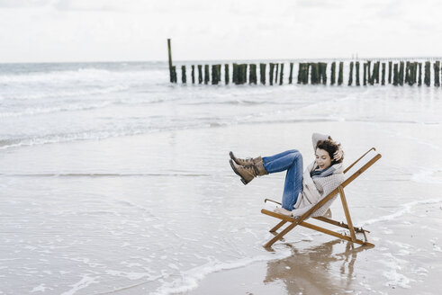 Frau sitzt auf einem Liegestuhl am Strand und hebt ihre Beine hoch - KNSF02572