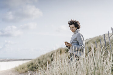 Woman standing in beach dune using cell phone - KNSF02576