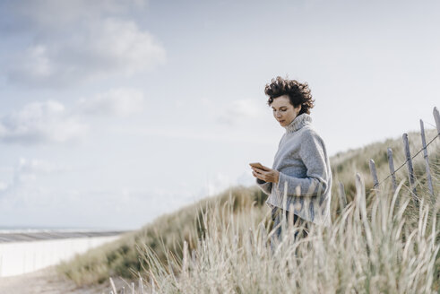 Frau steht in einer Stranddüne und benutzt ein Mobiltelefon - KNSF02576