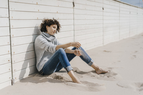 Frau sitzt am Strand und lehnt sich an eine Holzwand, lizenzfreies Stockfoto