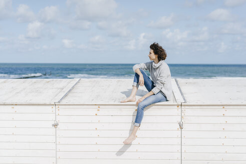 Woman sitting on wooden box on the beach - KNSF02584