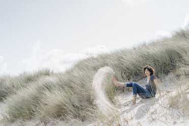 Playful woman sitting in beach dune - KNSF02592