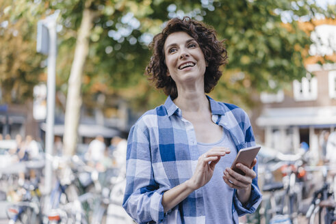 Glückliche Frau mit Mobiltelefon in der Stadt - KNSF02594