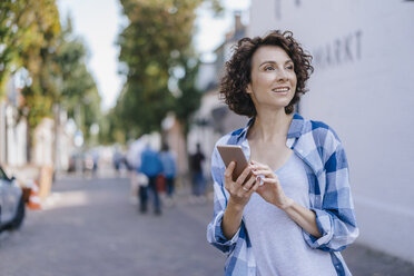 Lächelnde Frau mit Mobiltelefon in der Stadt - KNSF02596