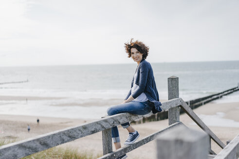 Porträt einer lächelnden Frau, die auf einem Geländer am Strand sitzt - KNSF02598