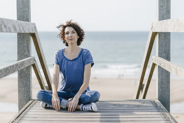 Portrait of woman sitting on boardwalk at the beach - KNSF02605