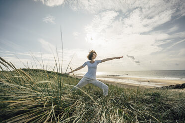 Woman practicing yoga in beach dune - KNSF02608