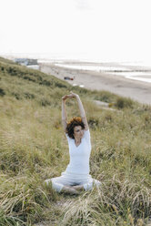 Woman stretching in beach dune - KNSF02618