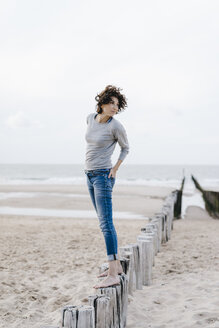 Frau steht auf einem Holzpfahl am Strand - KNSF02620