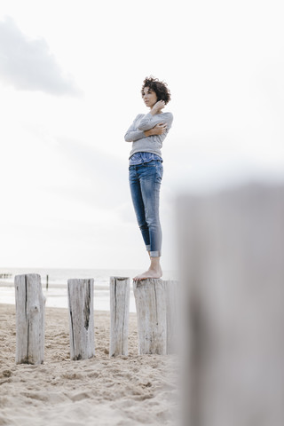 Frau steht auf einem Holzpfahl am Strand, lizenzfreies Stockfoto
