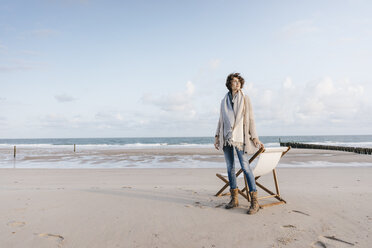 Woman standing next to deckchair on the beach - KNSF02631