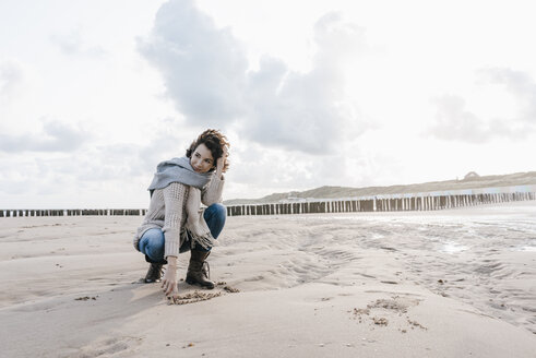 Frau hockt am Strand und zeichnet ein Herz in den Sand - KNSF02646