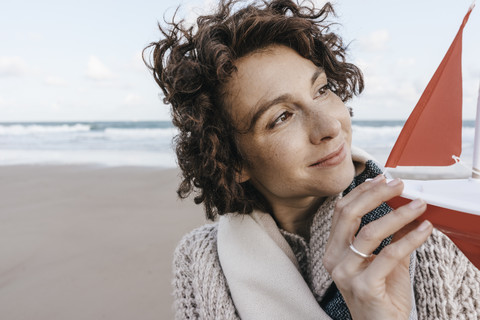 Porträt einer lächelnden Frau mit einem Spielzeugboot am Strand, lizenzfreies Stockfoto