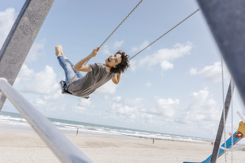 Glückliche Frau auf einer Schaukel am Strand, lizenzfreies Stockfoto