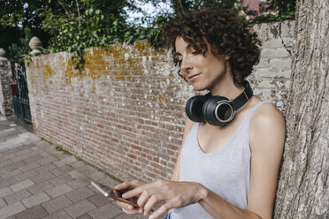Frau mit Kopfhörern und Mobiltelefon auf dem Bürgersteig - KNSF02682