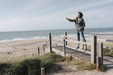 Frau steht auf der Promenade am Strand und macht ein Selfie - KNSF02688