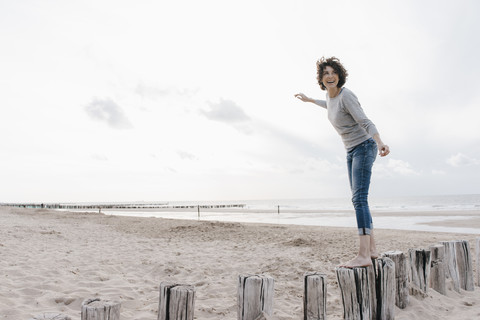 Glückliche Frau balanciert auf einem Holzpfahl am Strand, lizenzfreies Stockfoto