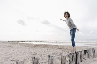 Glückliche Frau balanciert auf einem Holzpfahl am Strand - KNSF02698