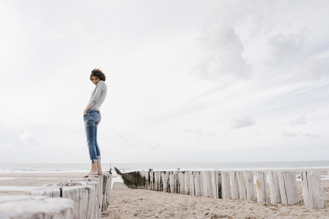 Frau steht auf einem Holzpfahl am Strand, lizenzfreies Stockfoto