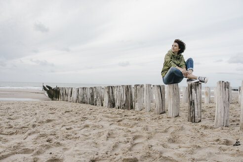 Frau sitzt auf einem Holzpfahl am Strand - KNSF02704