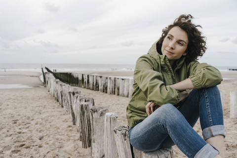 Frau sitzt auf einem Holzpfahl am Strand, lizenzfreies Stockfoto