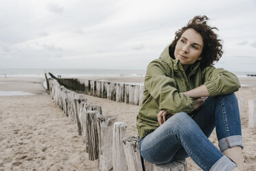 Frau sitzt auf einem Holzpfahl am Strand - KNSF02705