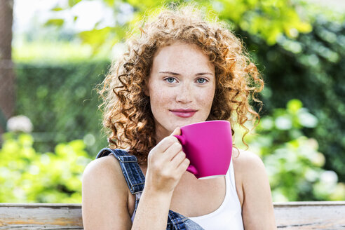 Portrait of redheaded young woman with pink coffee cup - FMKF04426