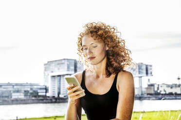 Deutschland, Köln, Porträt einer ernsten jungen Frau, die auf ihr Handy schaut - FMKF04431