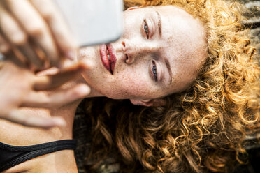 Portrait of redheaded young woman lying on bench using cell phone - FMKF04435