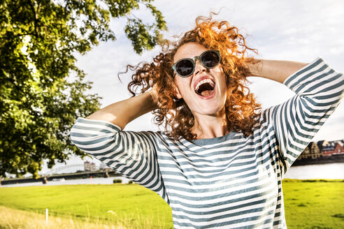 Germany, Cologne, portrait of screaming redheaded young woman wearing sunglasses - FMKF04440