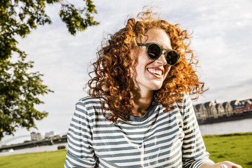 Deutschland, Köln, Porträt einer lachenden rothaarigen jungen Frau mit Sonnenbrille - FMKF04441