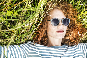 Portrait of young woman relaxing on a meadow wearing sunglasses - FMKF04444