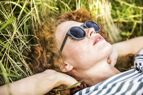 Junge Frau mit Sonnenbrille entspannt auf einer Wiese - FMKF04445