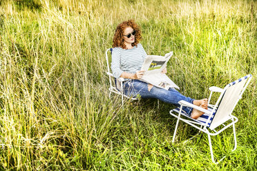 Young woman relaxing on a meadow reading newspaper - FMKF04449