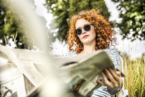 Porträt einer jungen Frau, die sich auf einer Wiese ausruht und Zeitung liest - FMKF04450