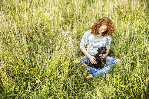 Junge Frau entspannt sich auf einer Wiese mit ihrem Hund - FMKF04451