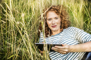 Porträt einer lächelnden jungen Frau, die sich auf einer Wiese mit einem Tablet entspannt - FMKF04452