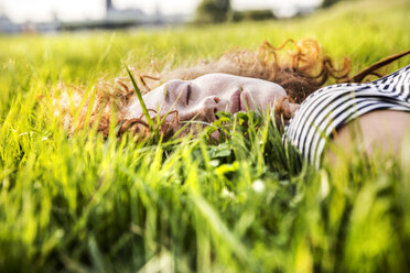 Porträt einer rothaarigen jungen Frau mit geschlossenen Augen auf einer Wiese liegend - FMKF04460